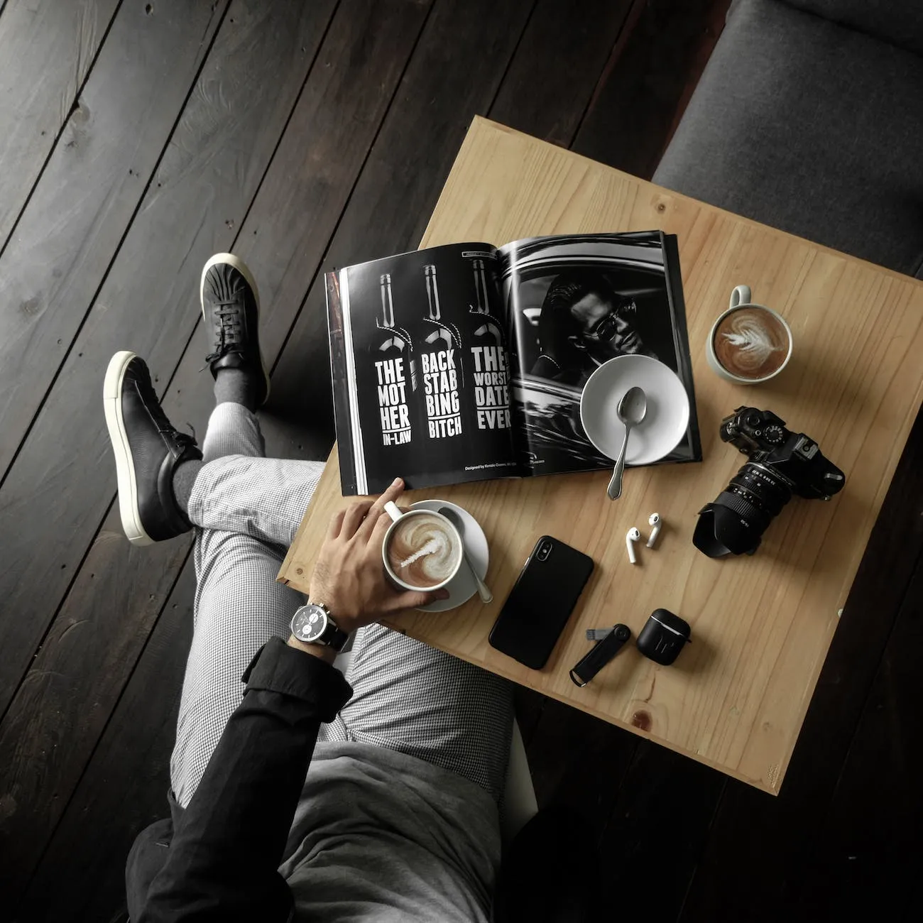 Vue de dessus d'une table avec un homme tenant une tasse de café au lait avec un magazine, un appareil photo, un téléphone portable et d'autres effets personnels